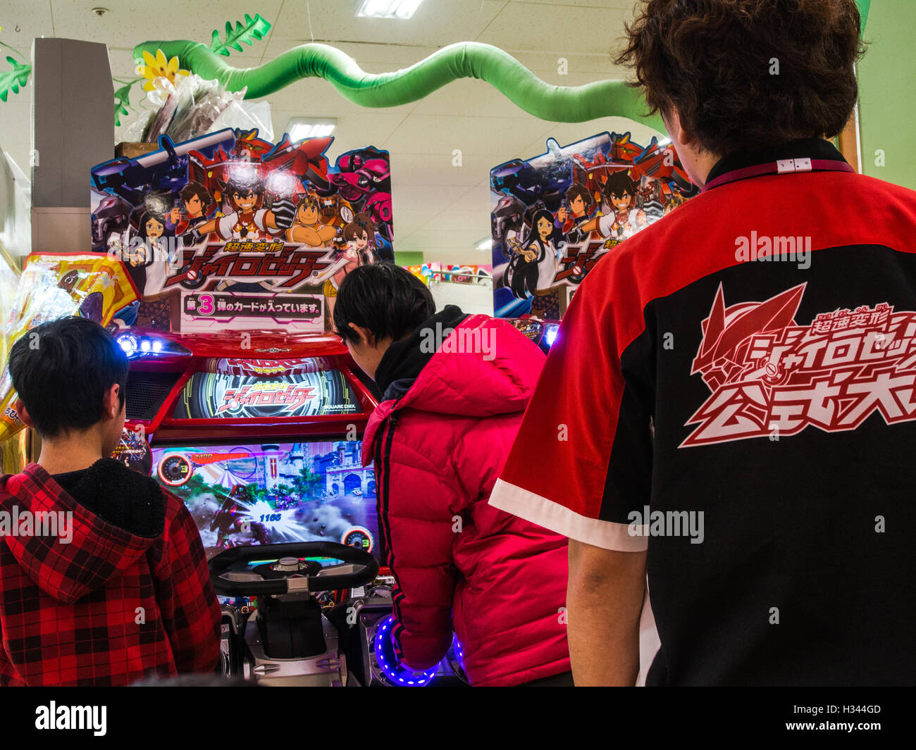 Boys, watched by uniformed attendant playing  video game slot machine, department store game arcade. AEON, Nisshin,Saitama Japan Stock Photo