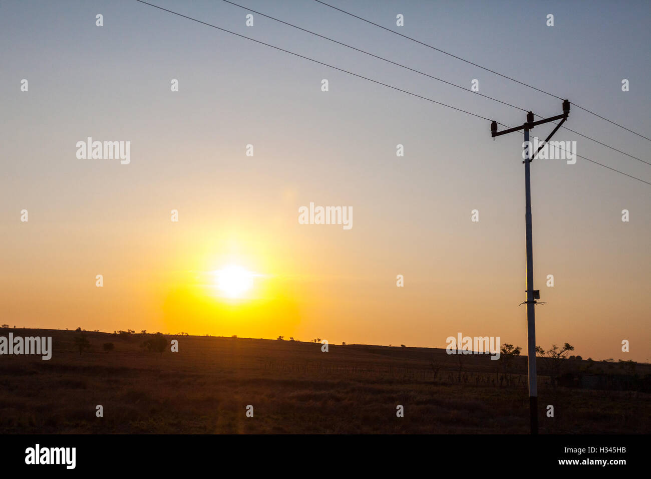 Sunset in a foreground of savanna and an electricity post during dry season in Kanatang, East Sumba, East Nusa Tenggara, Indonesia. Stock Photo