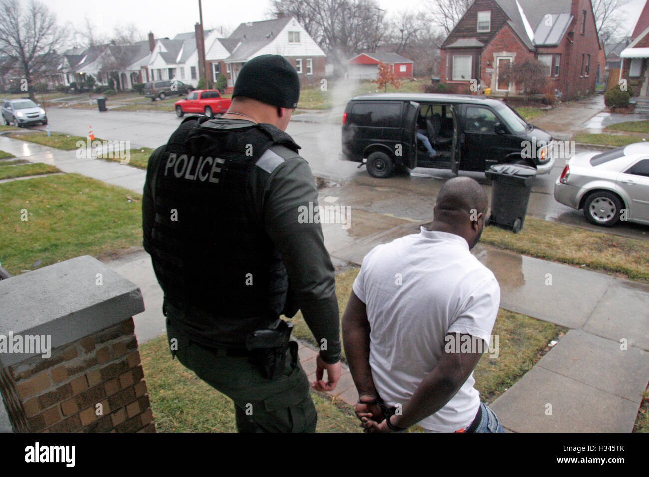 Police take away a handcuffed man after rading a suspected drug house in Detroit, Michigan, USA Stock Photo