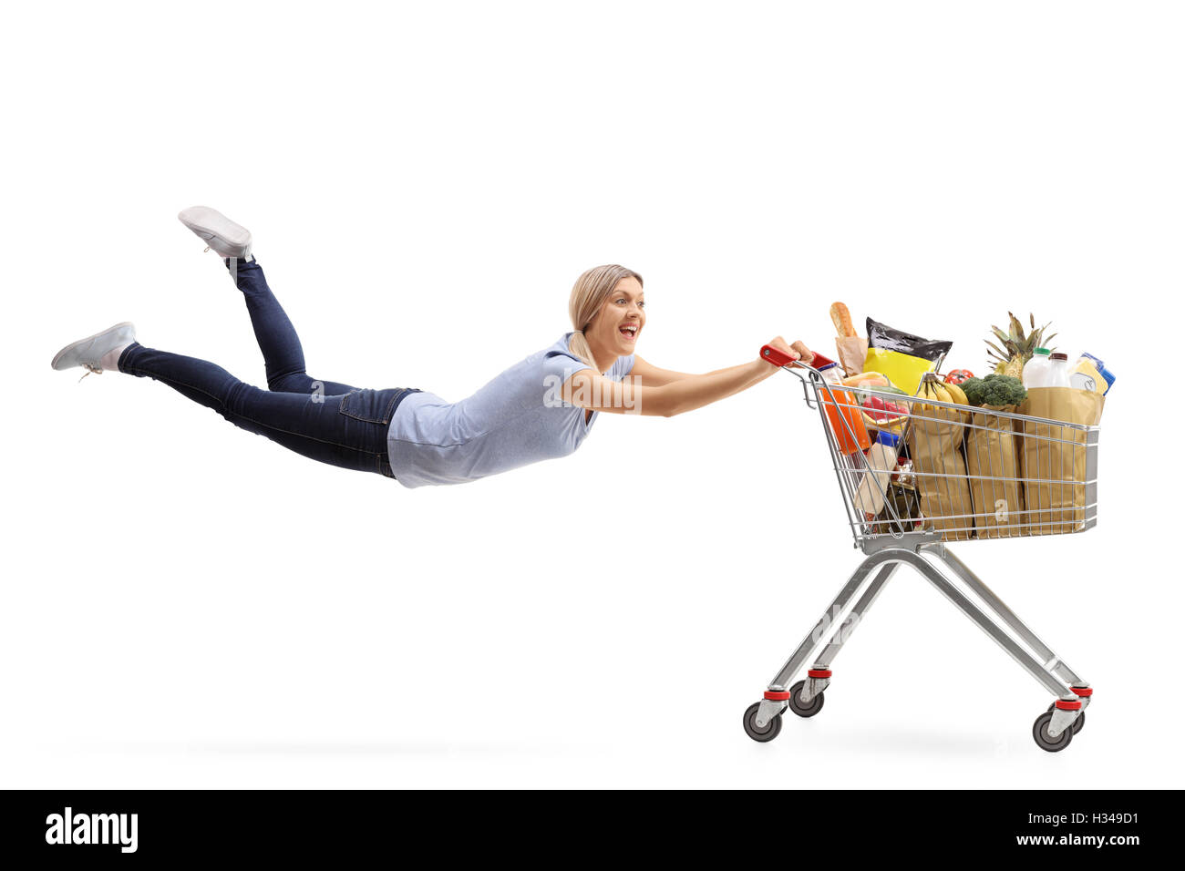 Happy woman being pulled by a shopping cart full of groceries isolated on white background Stock Photo
