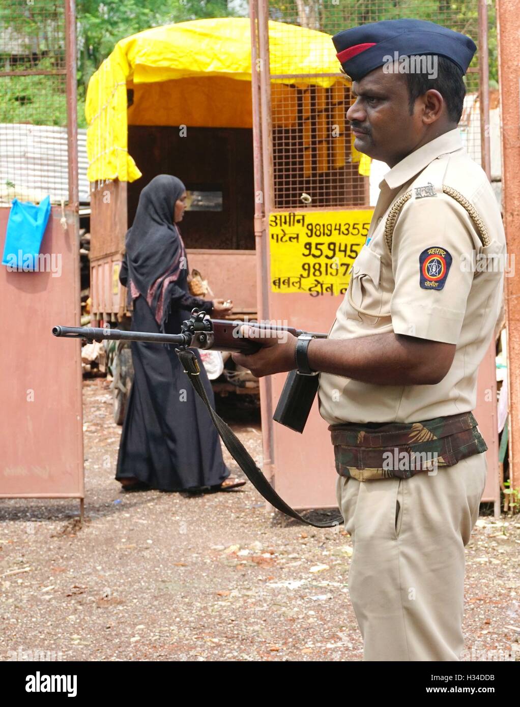 A burkha-clad Muslim woman walks past armed policeman conducting search combing operation slum area Uran 47 km East Mumbai Stock Photo