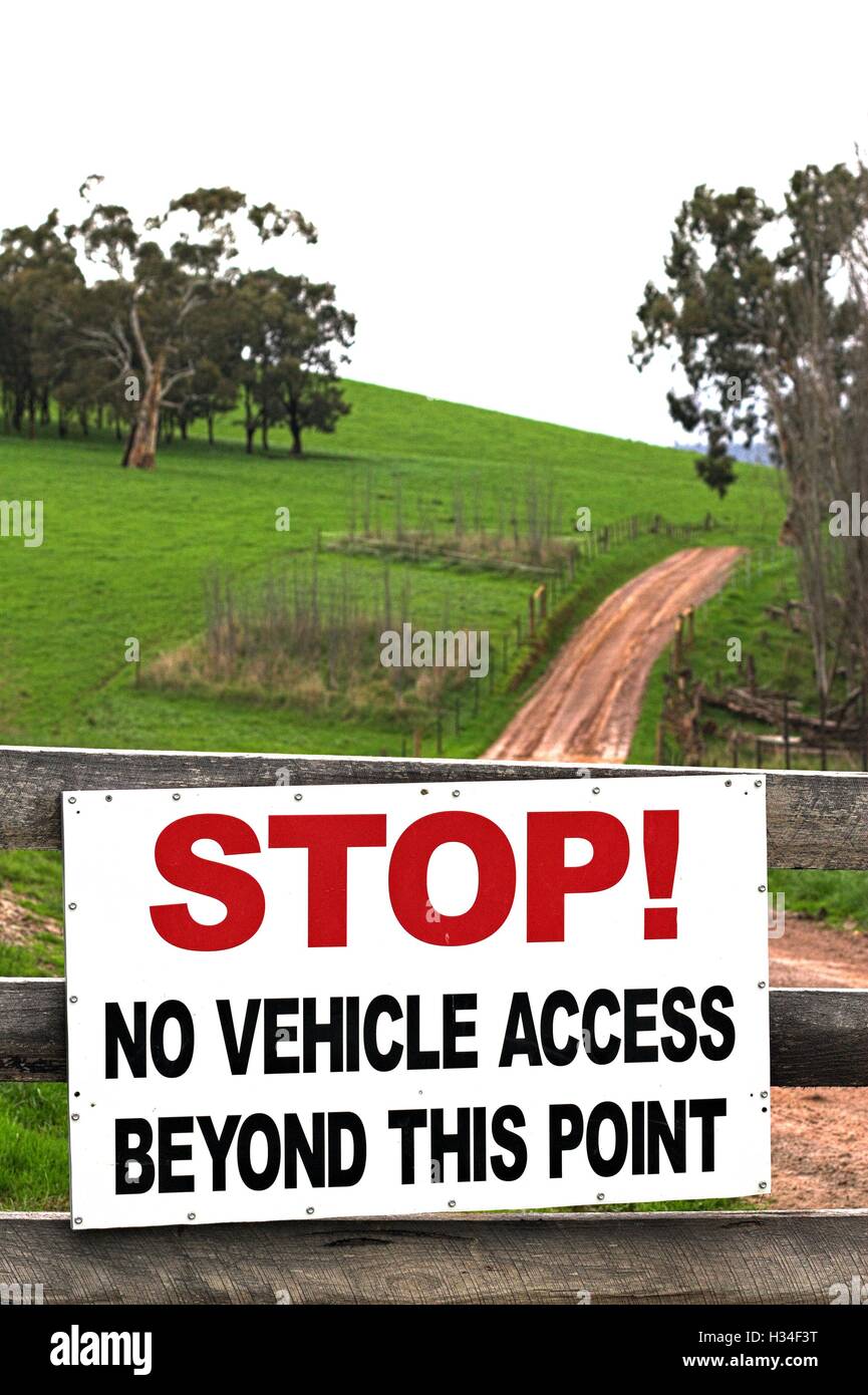 Large stop sign on a farm gate, stating no vehicle access beyond this point, with dirt road continuing in the distance. Stock Photo