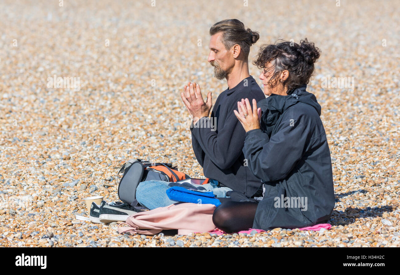 Couple sitting on a beach meditating in a praying lotus position. Stock Photo