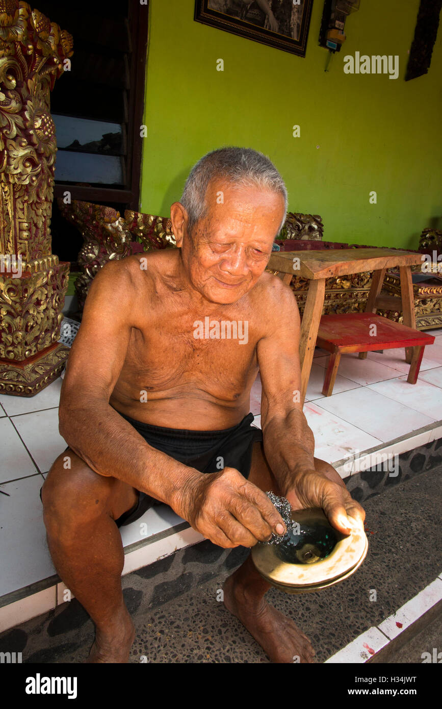 Indonesia, Bali, Lovina, Anturan, old gamelan maker polishing brass gong in village workshop Stock Photo