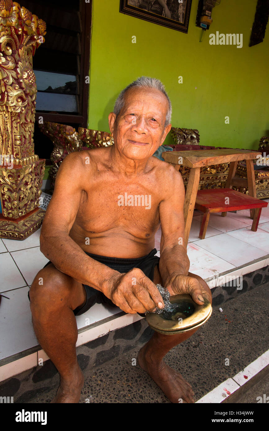 Indonesia, Bali, Lovina, Anturan, old gamelan maker polishing brass gong in village workshop Stock Photo