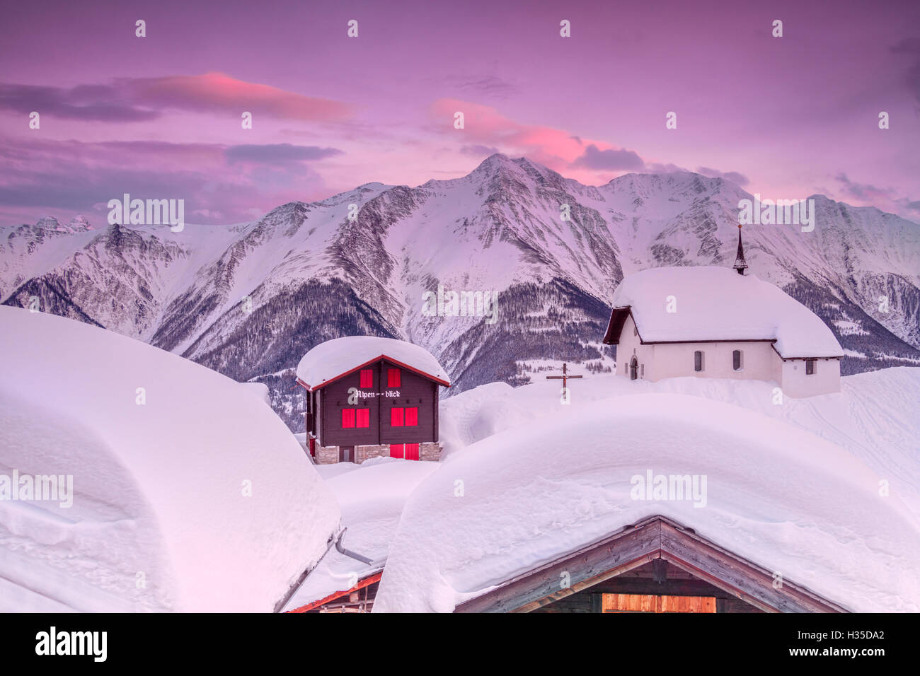Pink sky at sunset frames the snowy mountain huts and church, Bettmeralp, district of Raron, canton of Valais, Switzerland Stock Photo