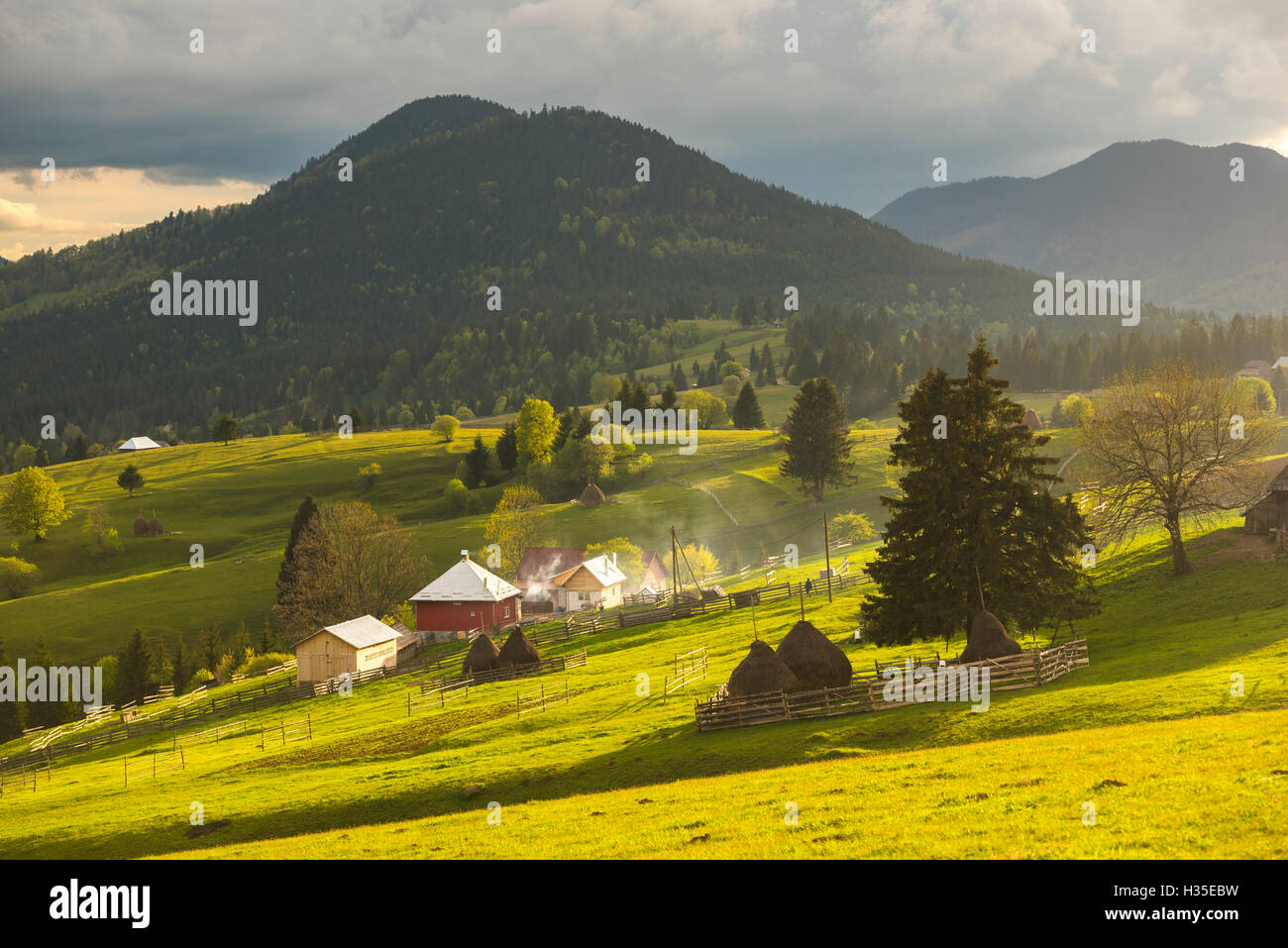 Farm and haystacks in the rural Transylvania landscape at sunset, Piatra Fantanele, Transylvania, Romania Stock Photo