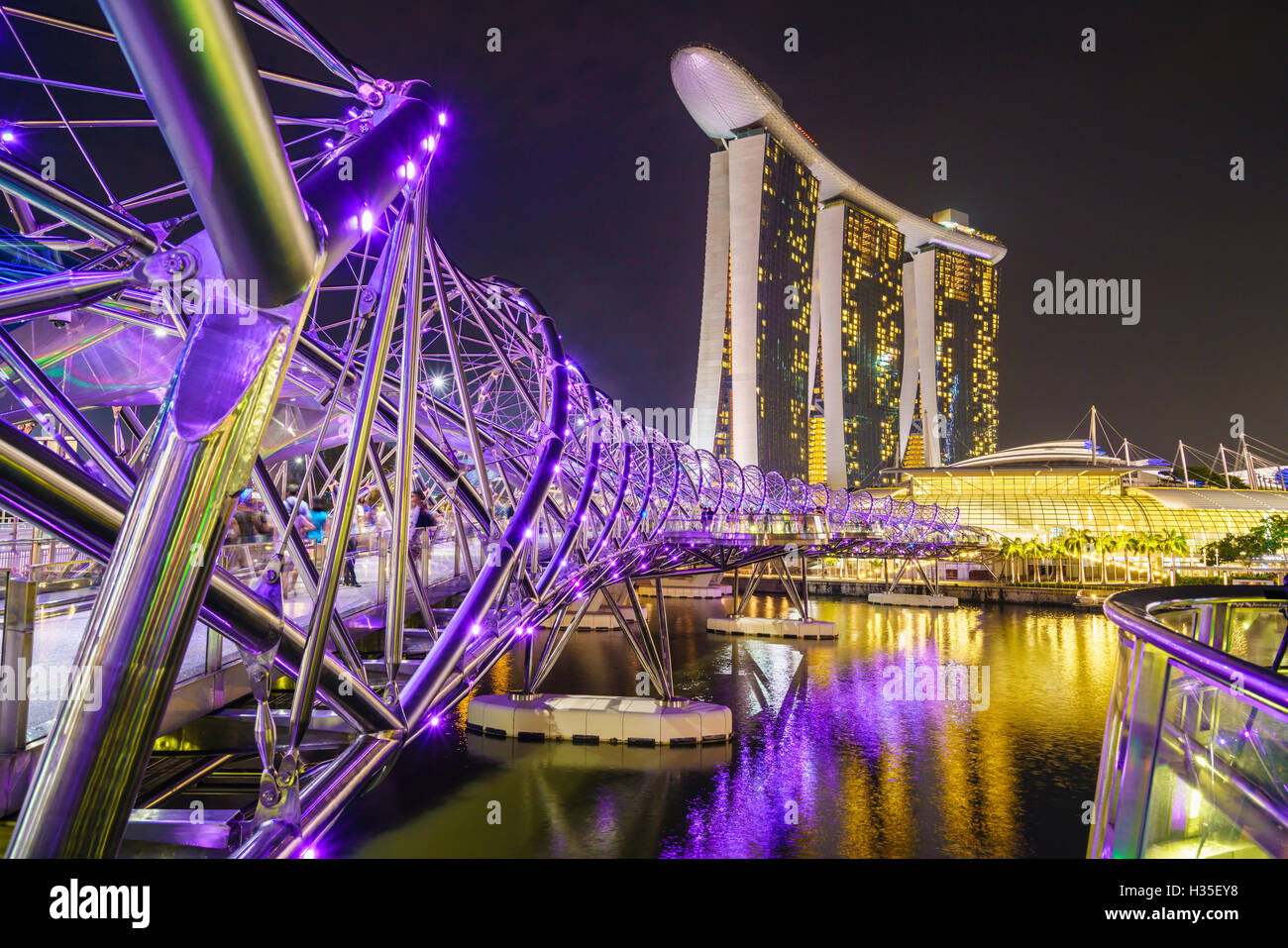 People strolling on the Helix Bridge towards the Marina Bay Sands and ArtScience Museum at night, Marina Bay, Singapore Stock Photo