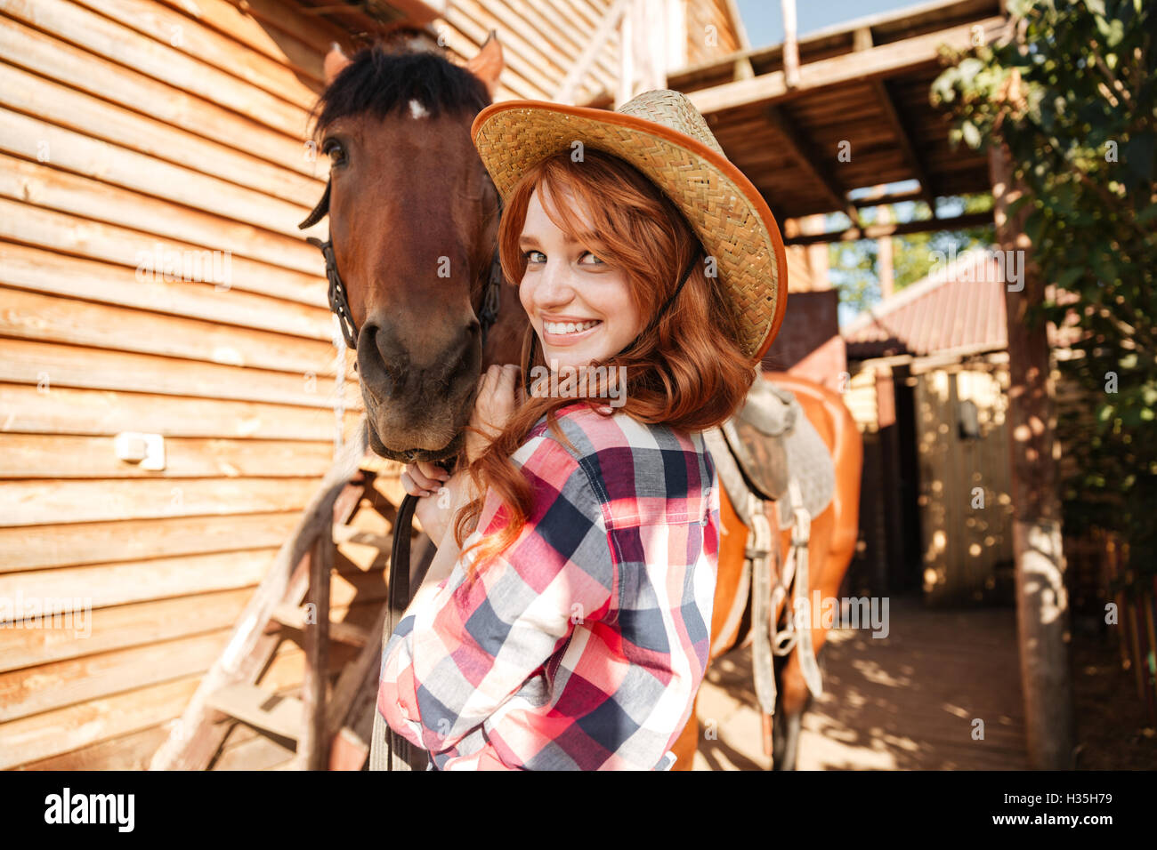 Closeup of cheerful cute young woman cowgirl in hat with horse Stock Photo