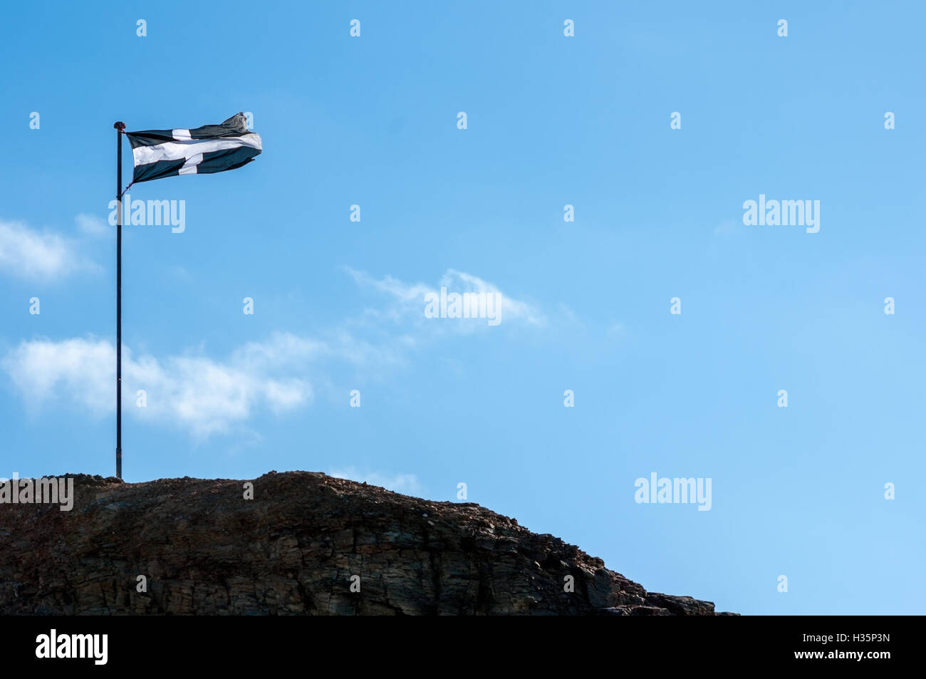 Cornish flag flying in the breeze on the rocks at Perranporth. Stock Photo