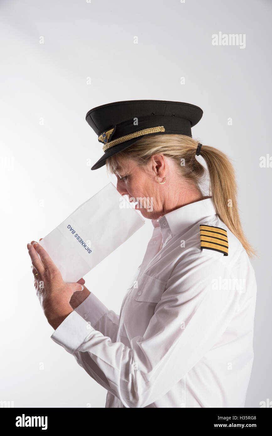 Woman using a sickness bag - A uniformed female pilot feeling nauseous using a paper air sickness bag Stock Photo