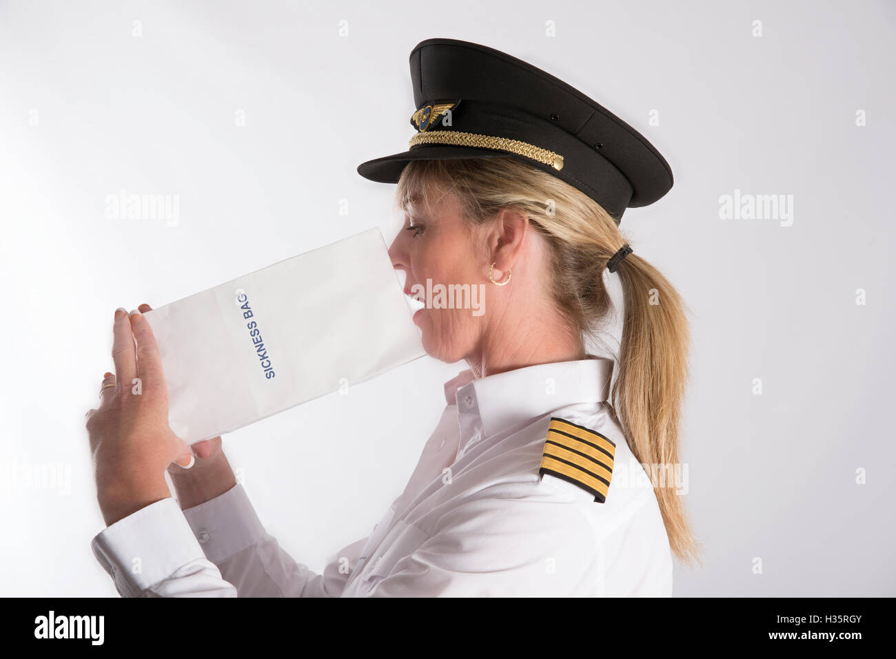 Woman using a sickness bag - A uniformed female pilot feeling nauseous using a paper air sickness bag Stock Photo