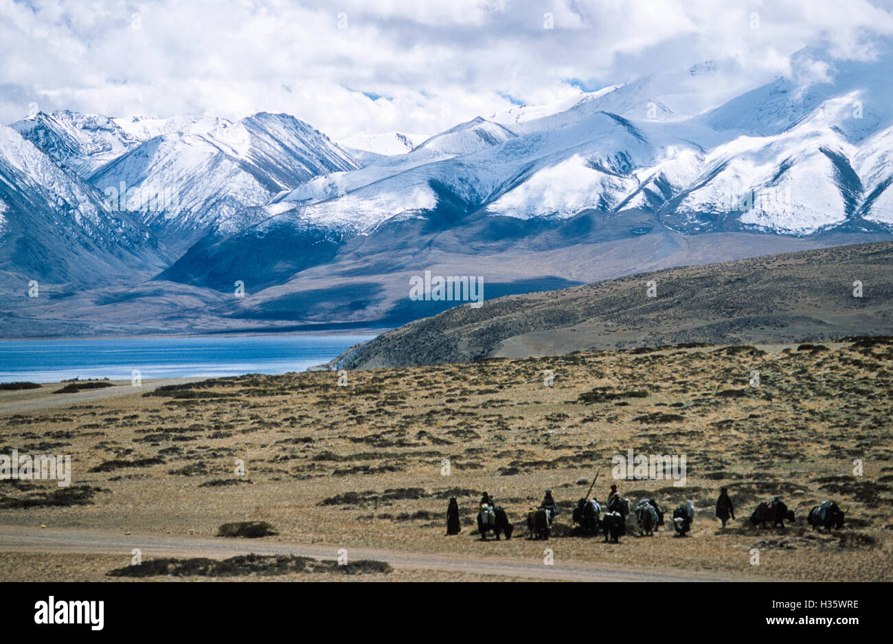 Group of Tibetans on a pilgrimage around Mount Kailash. Holy Lake Manasarovar and Gurla Mandhata mountain range south of the lake in the background. Stock Photo