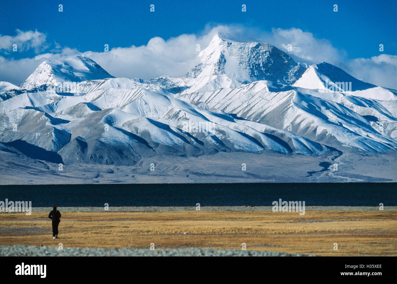 In  early  morning  light  a  western  visitor  walks  towards  Lake  Manasarovar  and  on  its  southern  shore  rises  Gurla Stock Photo