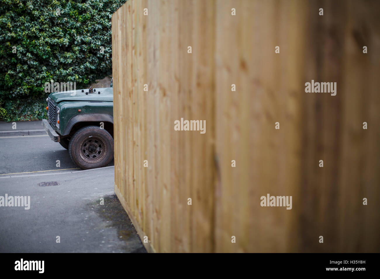 An old green land rover hidden behind a large wodden fence. Stock Photo