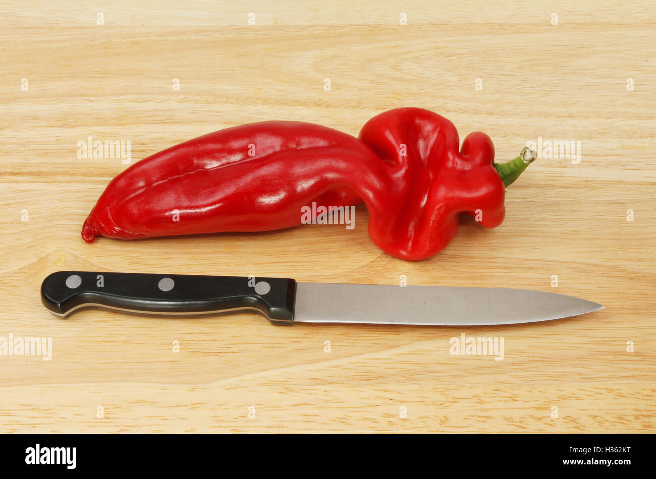 Pointed sweet red pepper and kitchen knife on a wooden chopping board Stock Photo