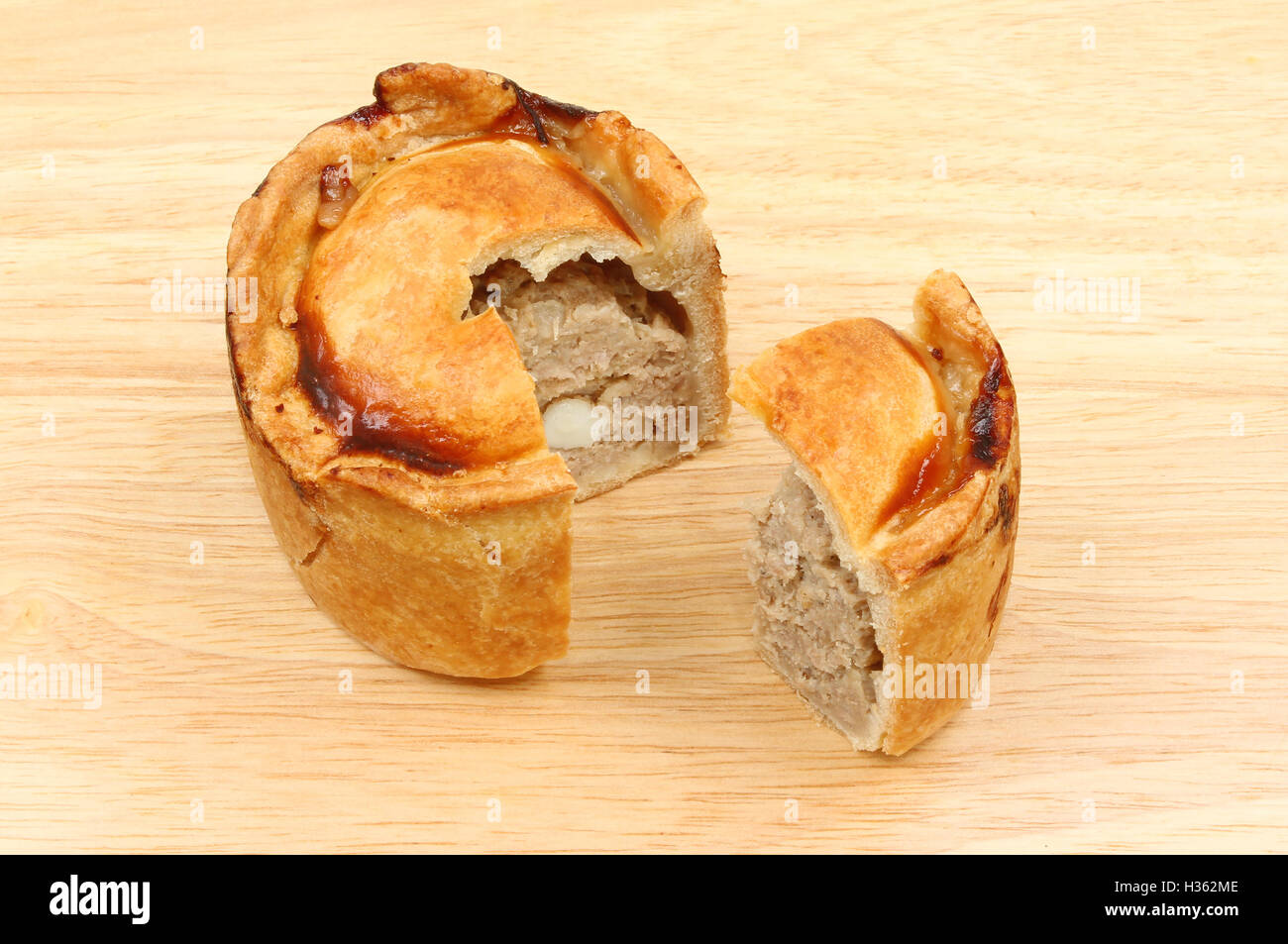 Handmade hot water pastry pork pie with a slive cut out on a wooden chopping board Stock Photo