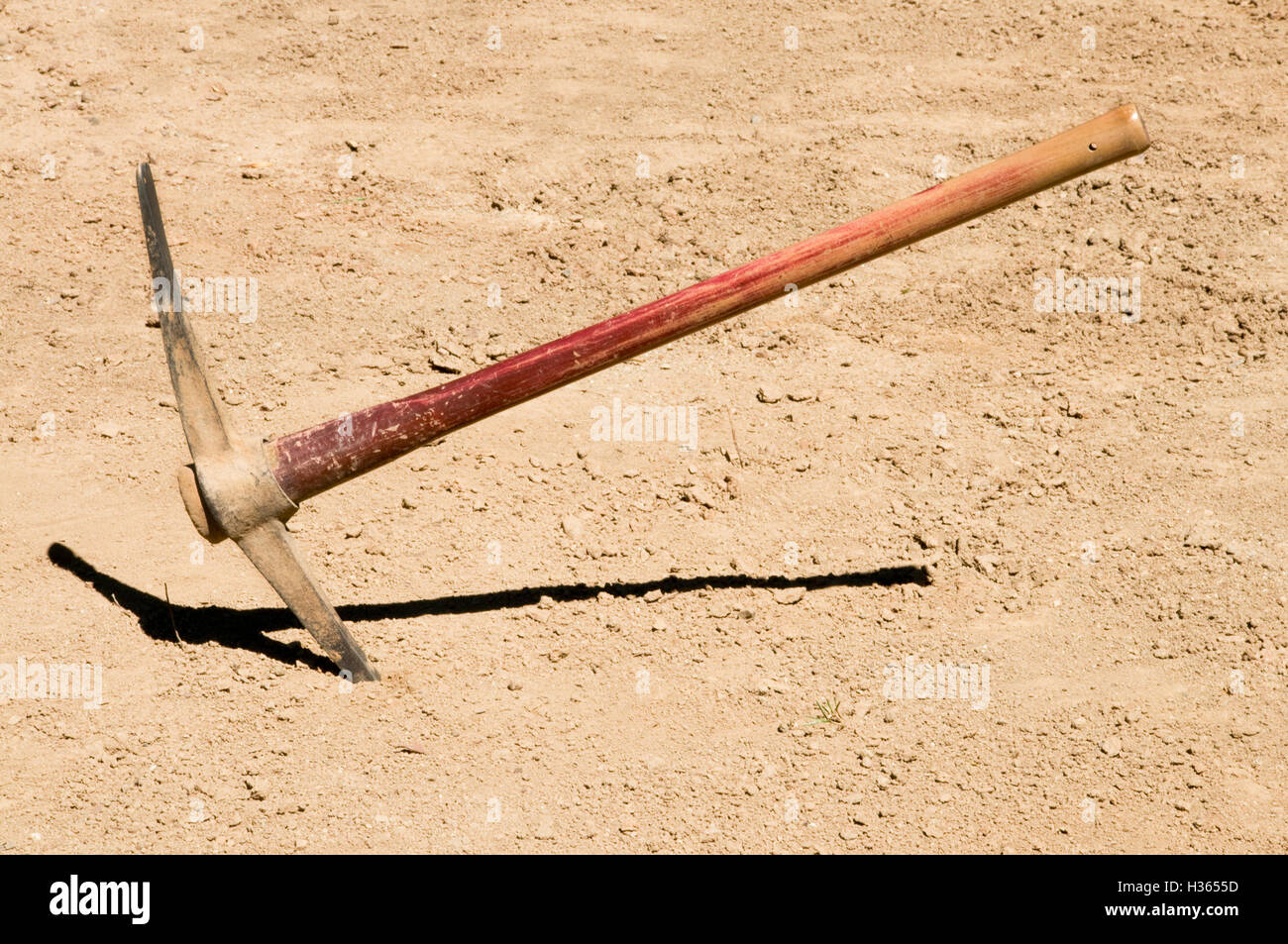 Worn distressed pick ax plunged into dirt ground Stock Photo