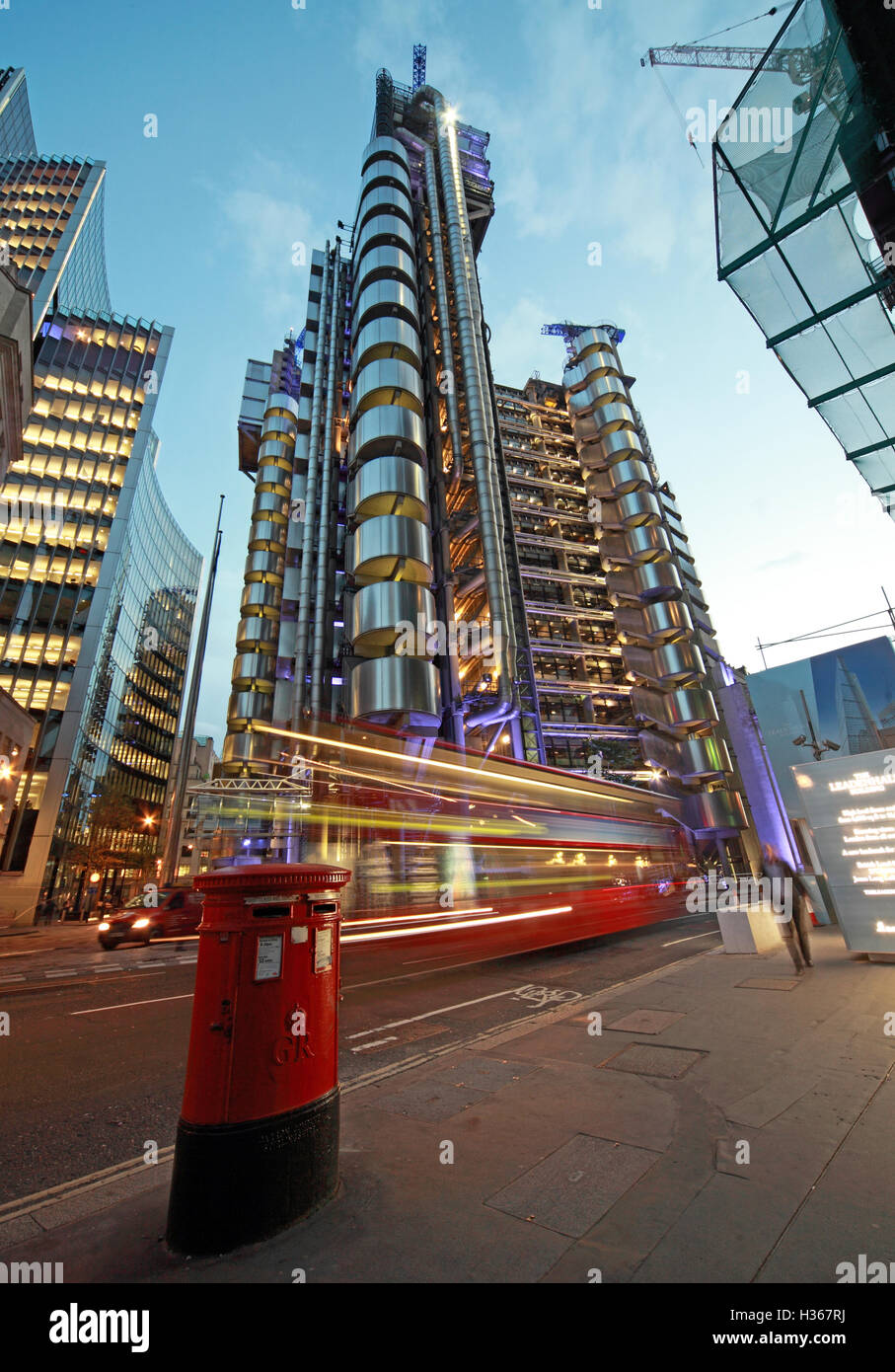 Red London bus passes Lloyd's building at dusk, Lime St, England Stock Photo