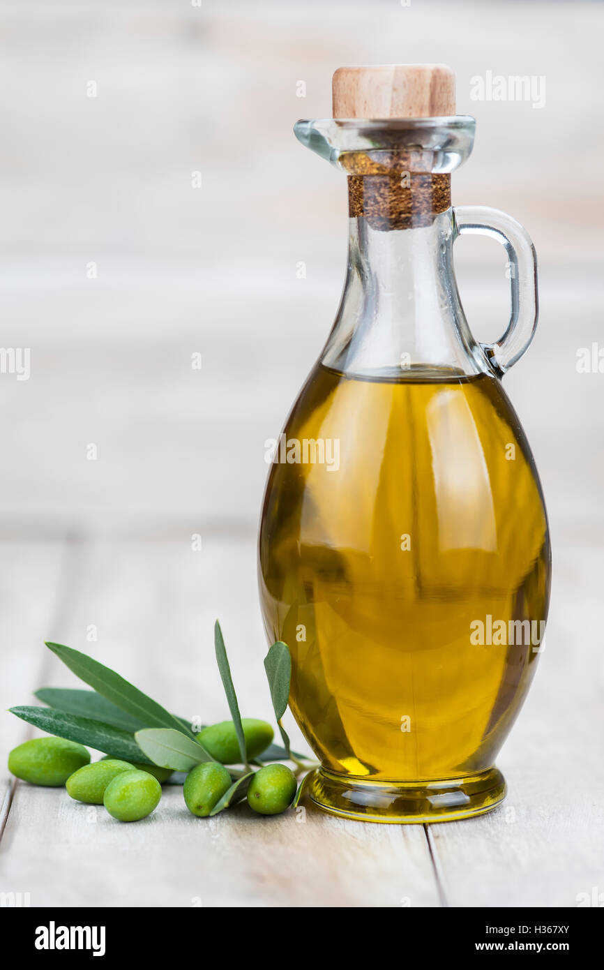A glass bottle of olive oil and green olives on a wooden background ...