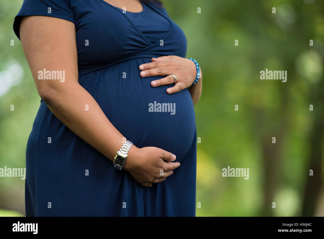 A heavily pregnant woman holds her stomach outdoors against a blurred background. Stock Photo