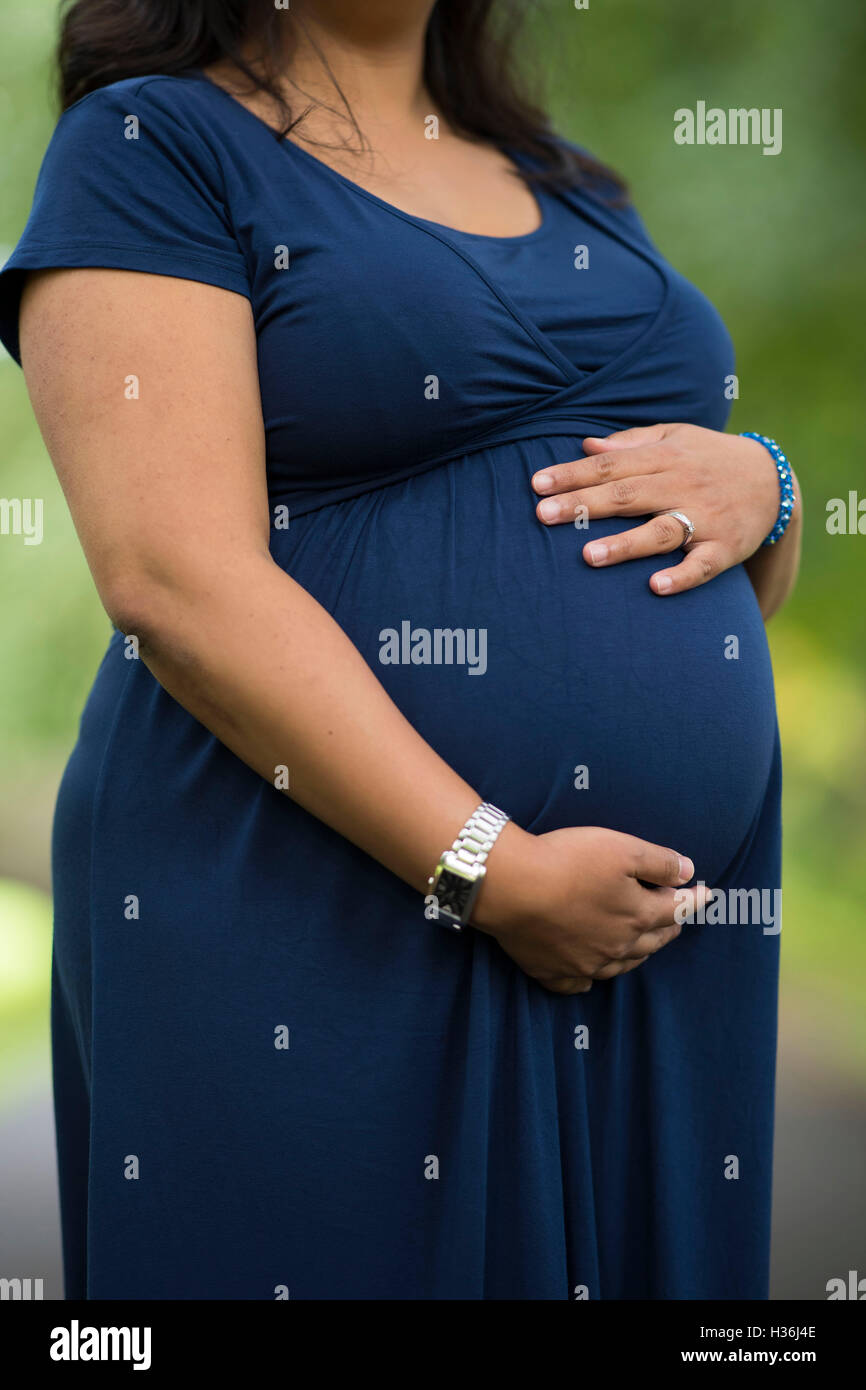 A heavily pregnant woman holds her stomach outdoors against a blurred background. Stock Photo
