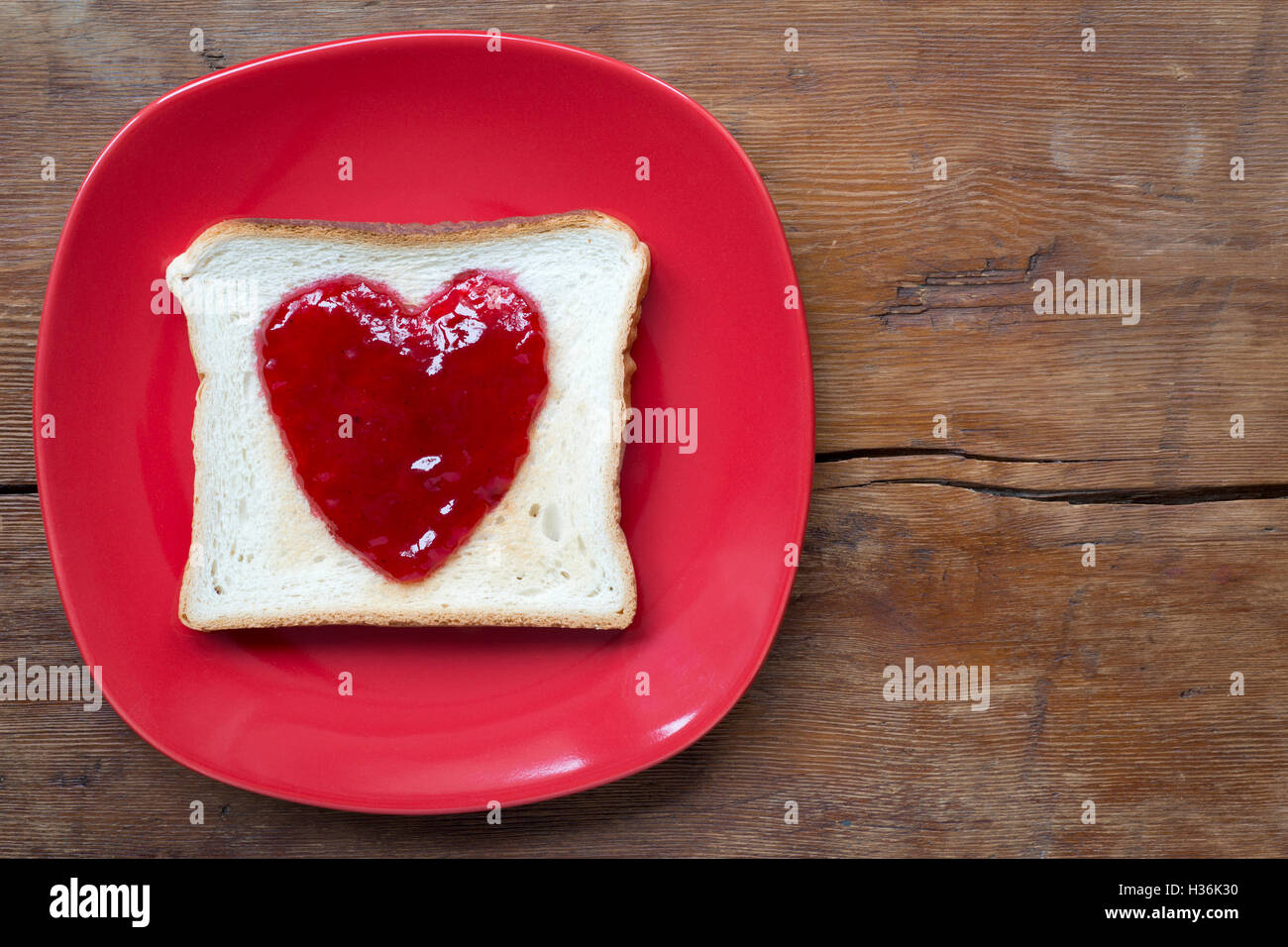 fried toast with heart jam on red plate on vintage wooden surface Stock Photo