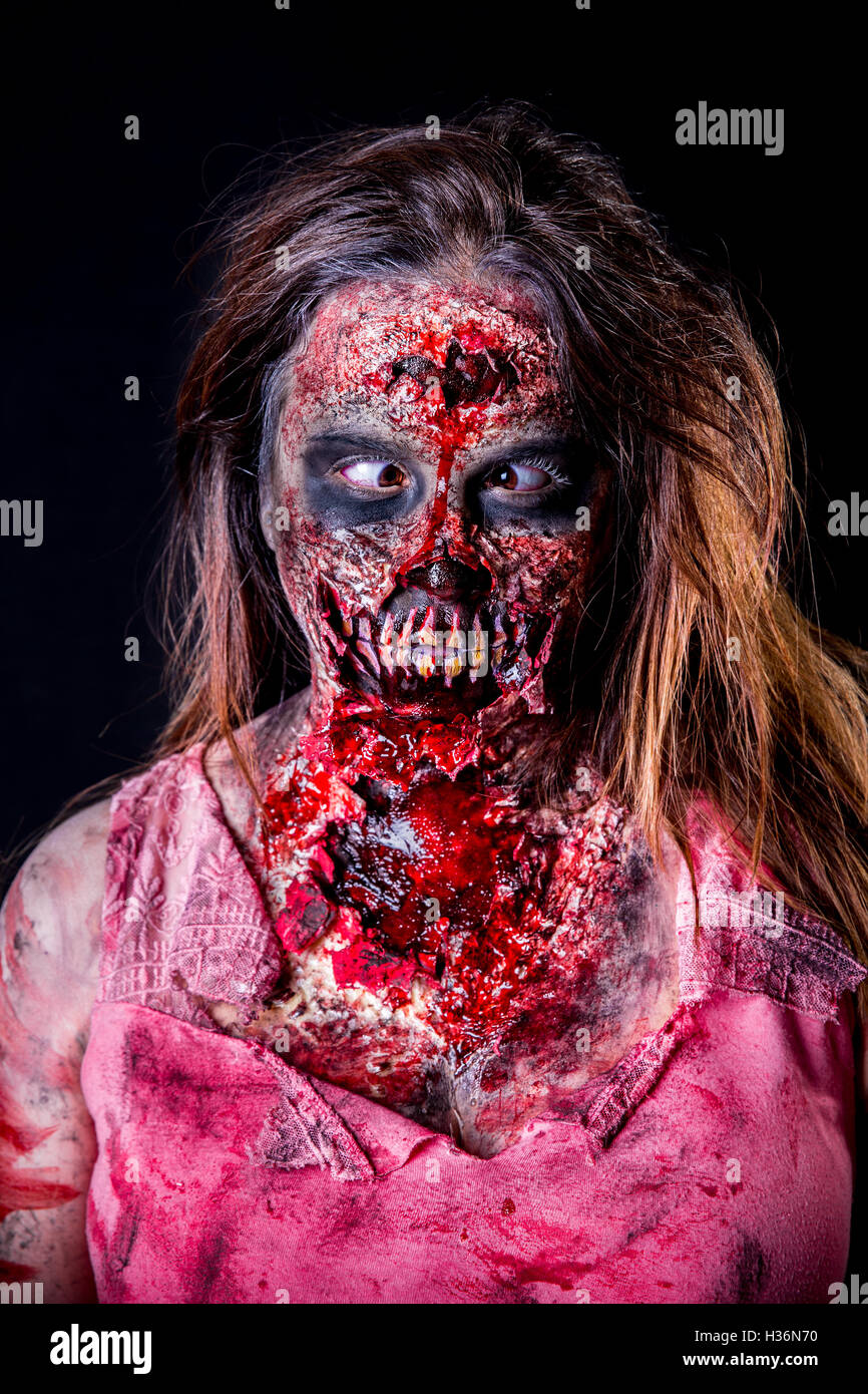Portrait of zombie girl with crossed eyed and bloody makeup with latex prosthesis. Stock Photo