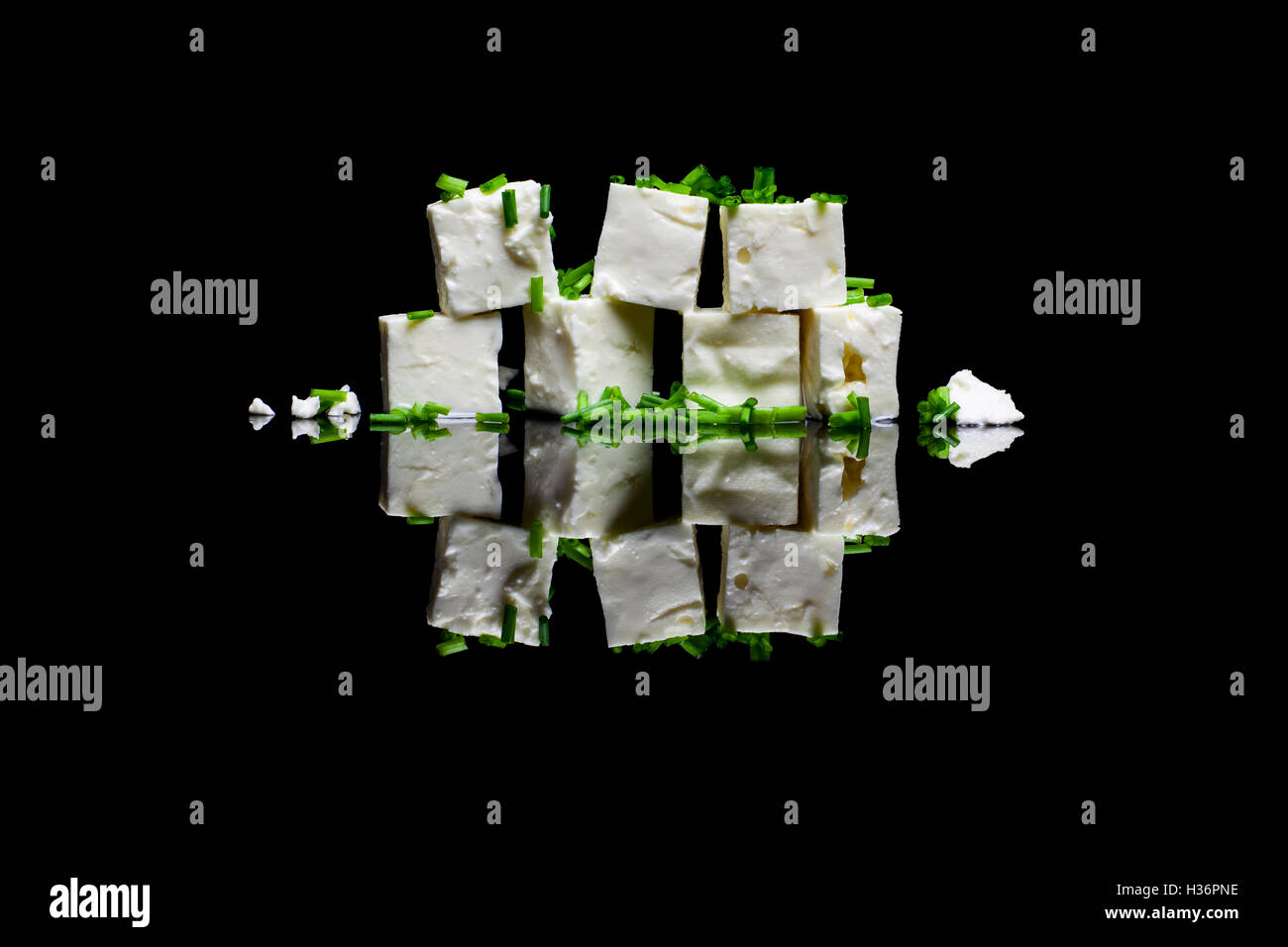 Seven blocks of feta cheese with green chive on black reflective