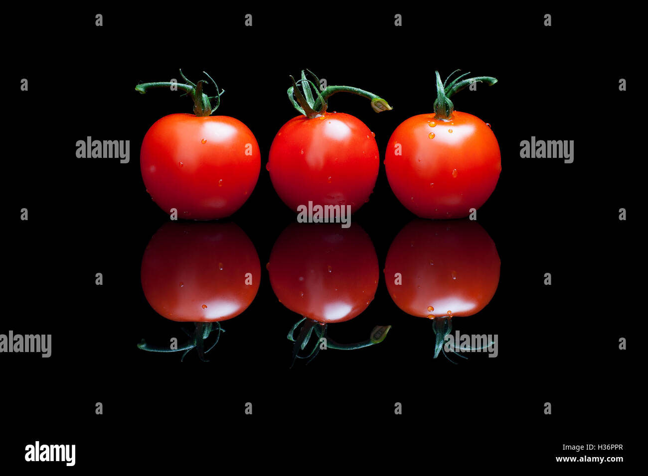Three tomatoes on a black shiny background Stock Photo