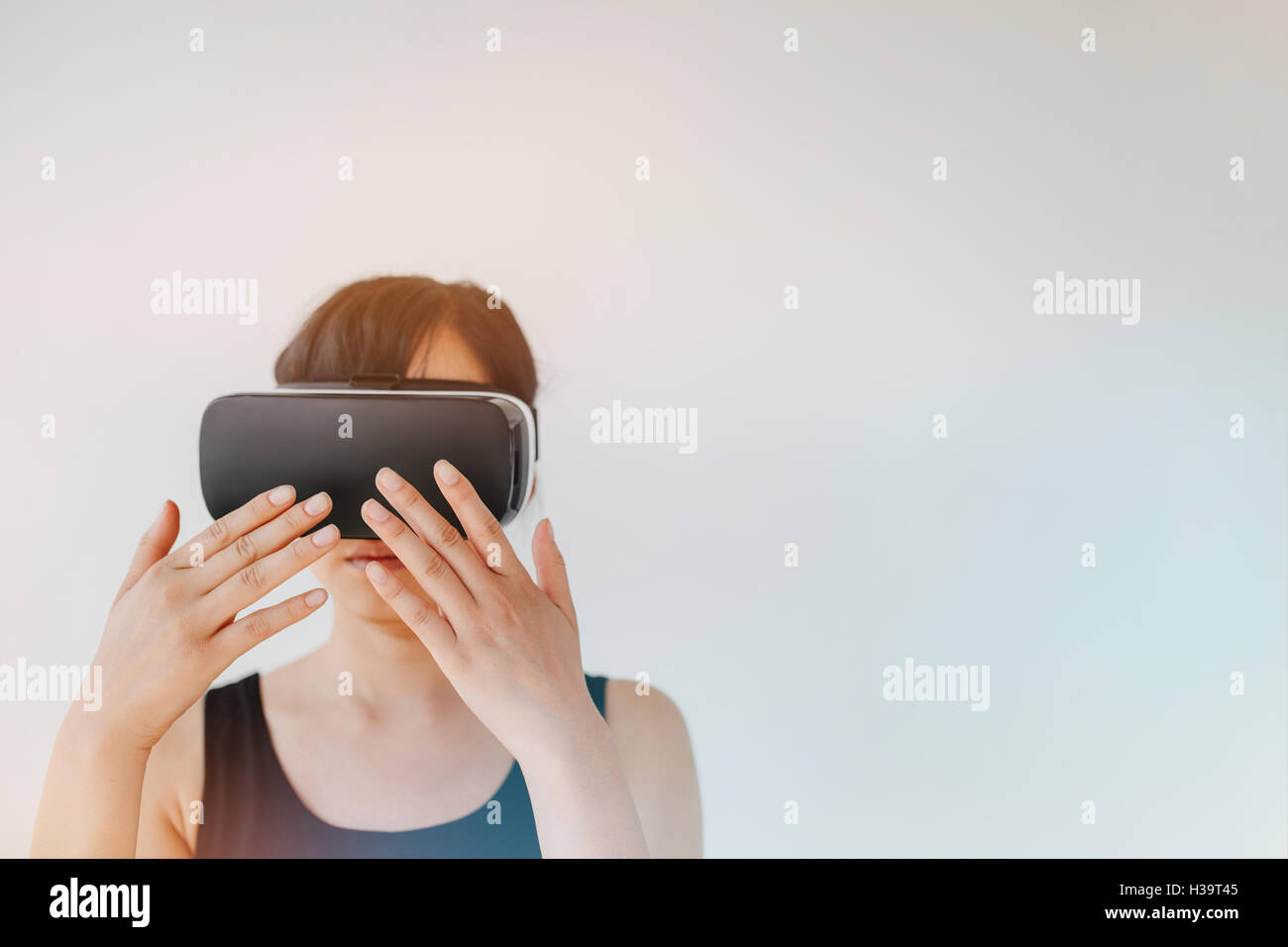 Shot of young woman wearing virtual reality goggle against grey background. Female with VR headset connecting device making gest Stock Photo