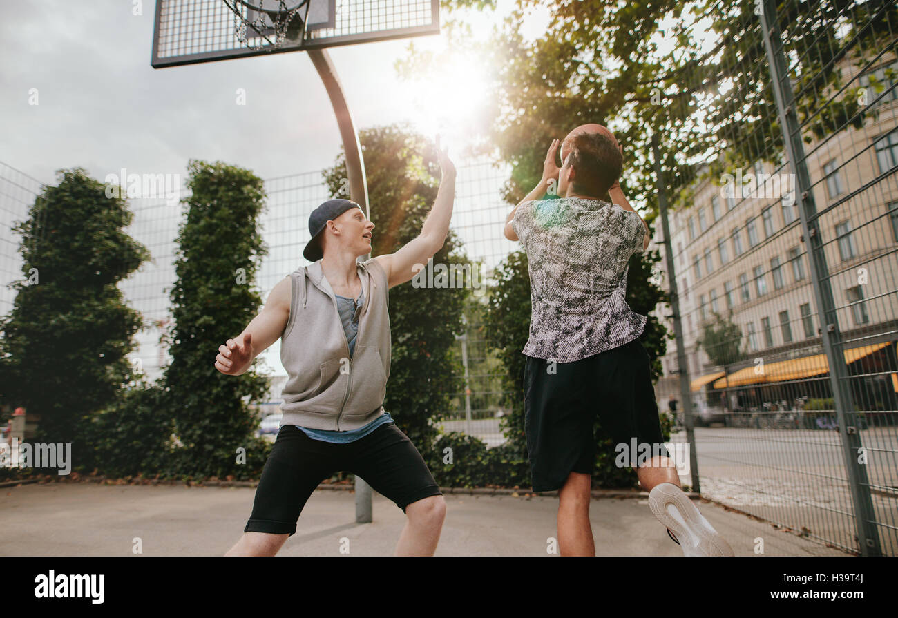Two young men playing basketball against each other. Teenage friends playing a game of basketball on an outdoor court. Stock Photo