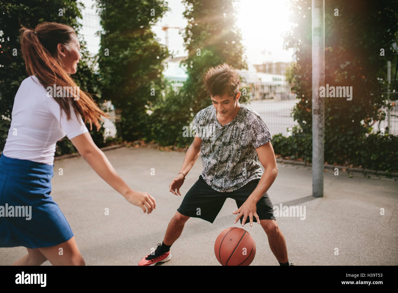 Two young man and woman on basketball court dribbling with ball. Friends playing basketball on court and having fun. Stock Photo