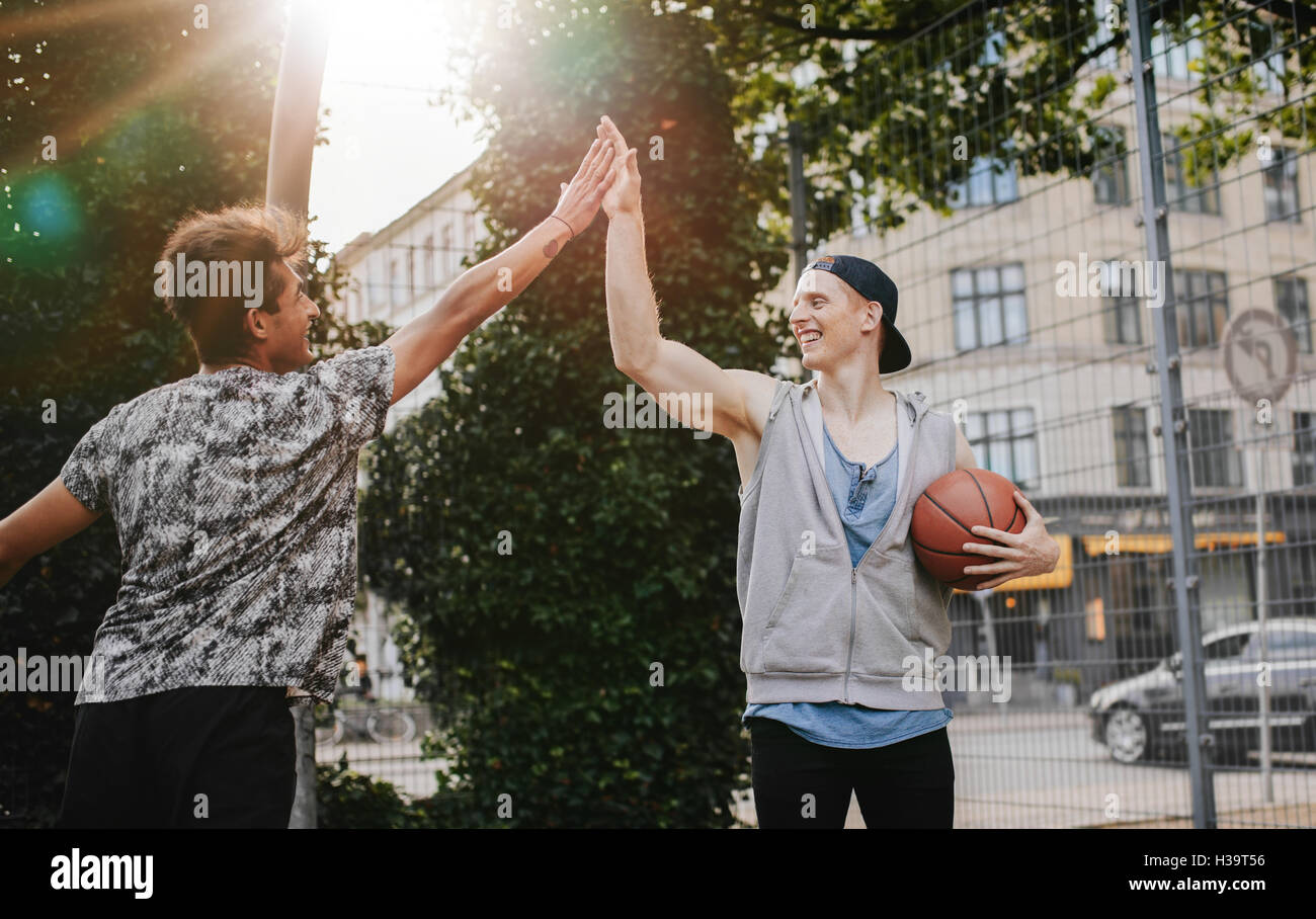Two young friends giving high five after a game of streetball. Teenage basketball players enjoying after a match. Stock Photo