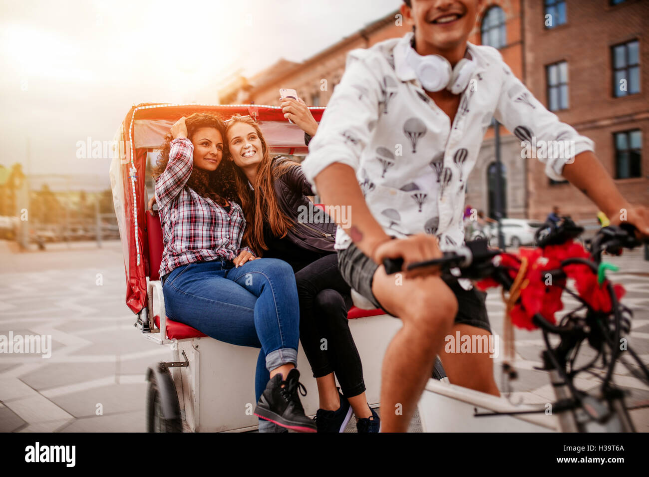 Shot of female friends taking selfie on tricycle. Young man riding tricycle bike with women sitting at back taking self portrait Stock Photo