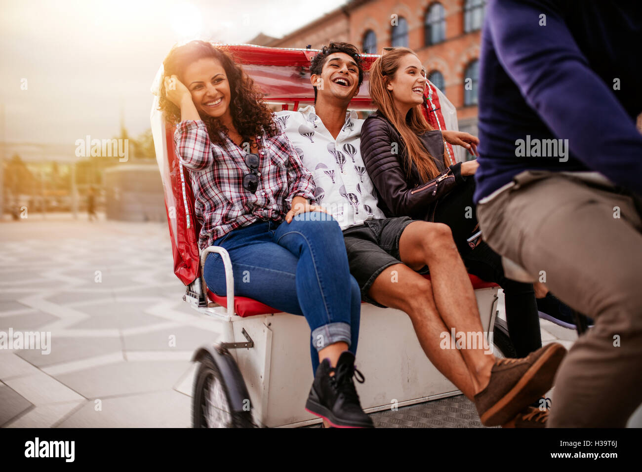 Teenage friends enjoying tricycle ride in the city. Teenagers riding on tricycle on road and smiling. Stock Photo