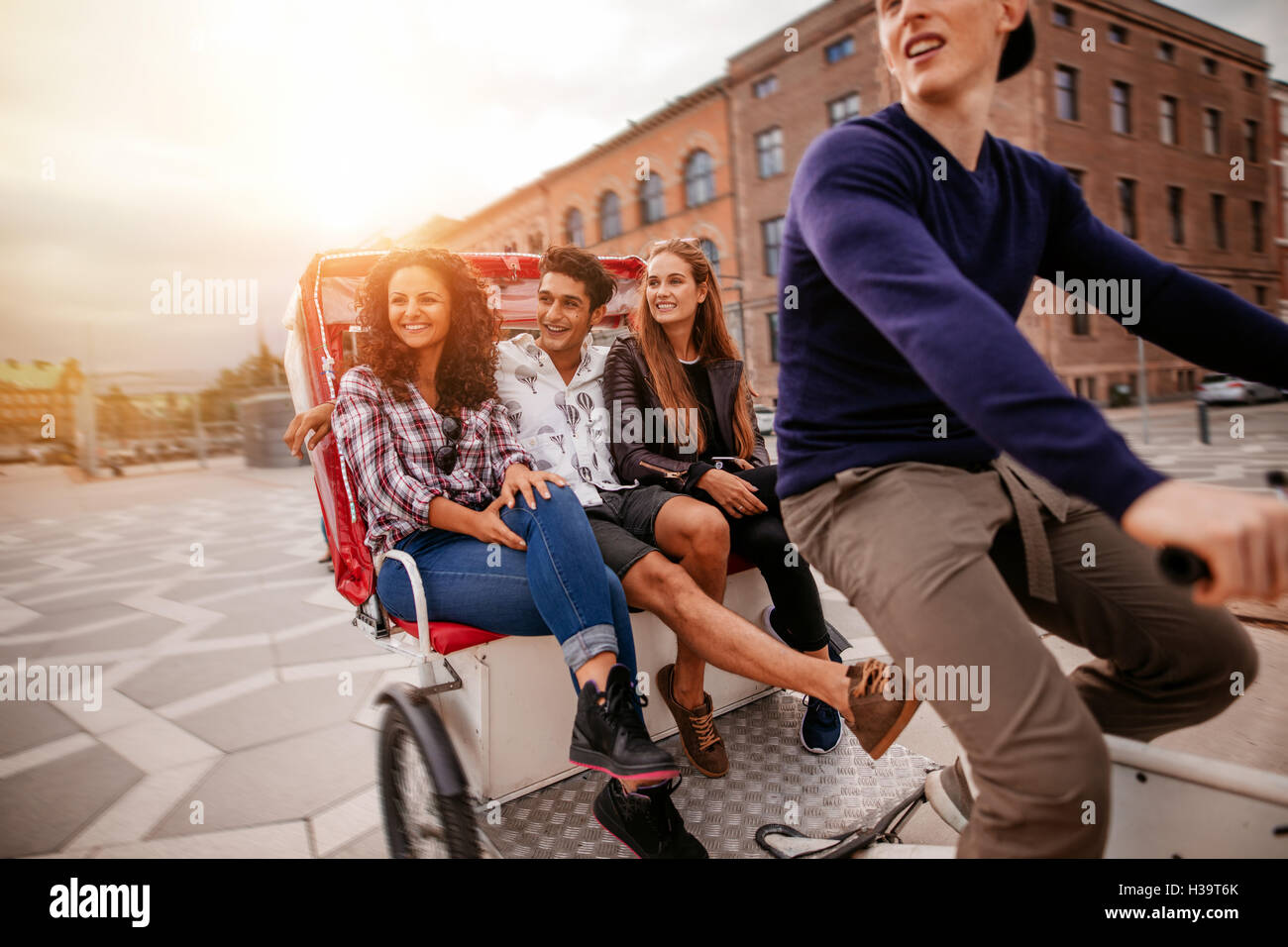 Group of teenagers traveling on tricycle in the city. Young men and women riding on tricycle on road. Stock Photo