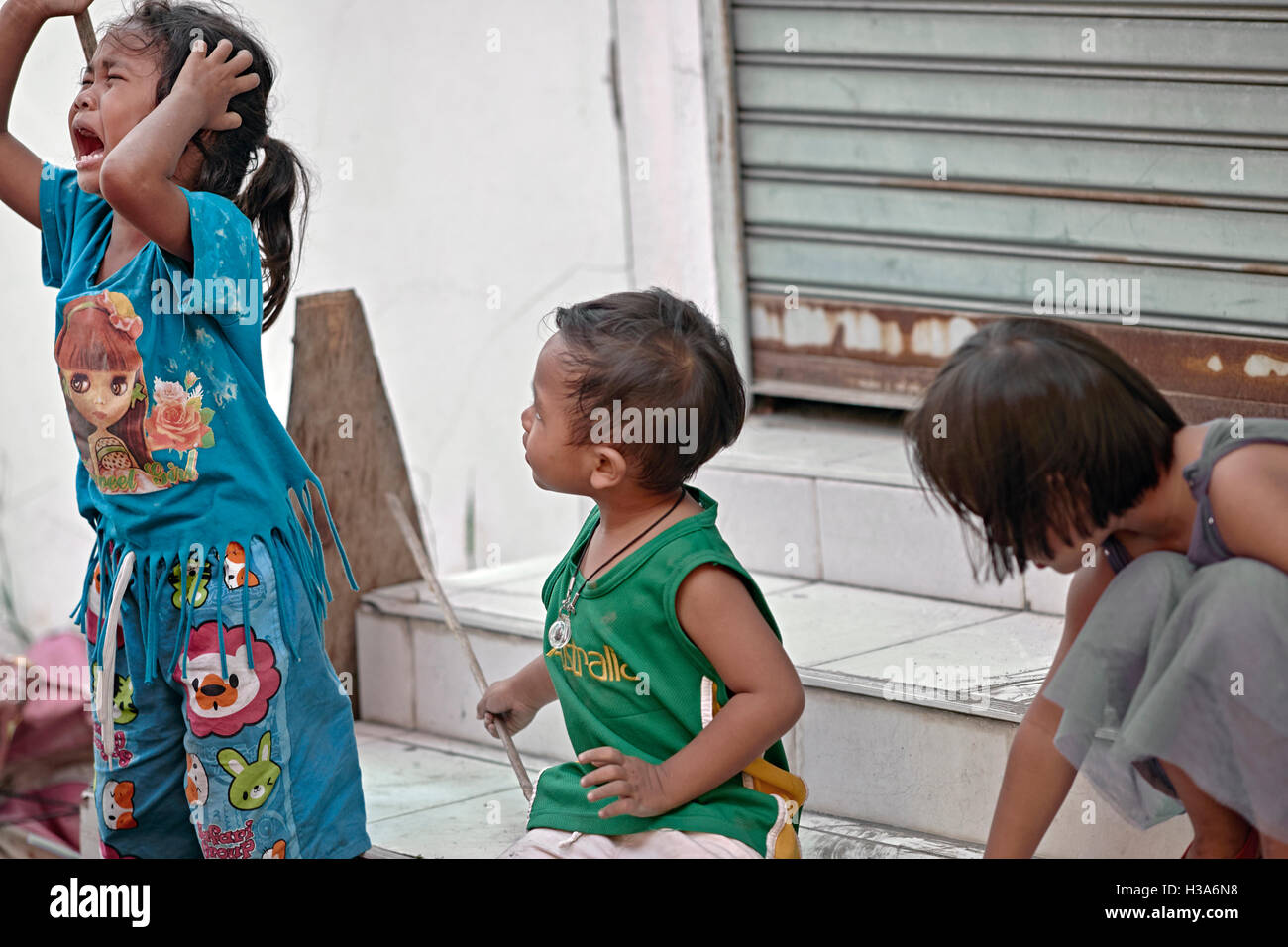 Thailand street altercation with young children and a crying sister having been struck with a stick by her young brother. Stock Photo