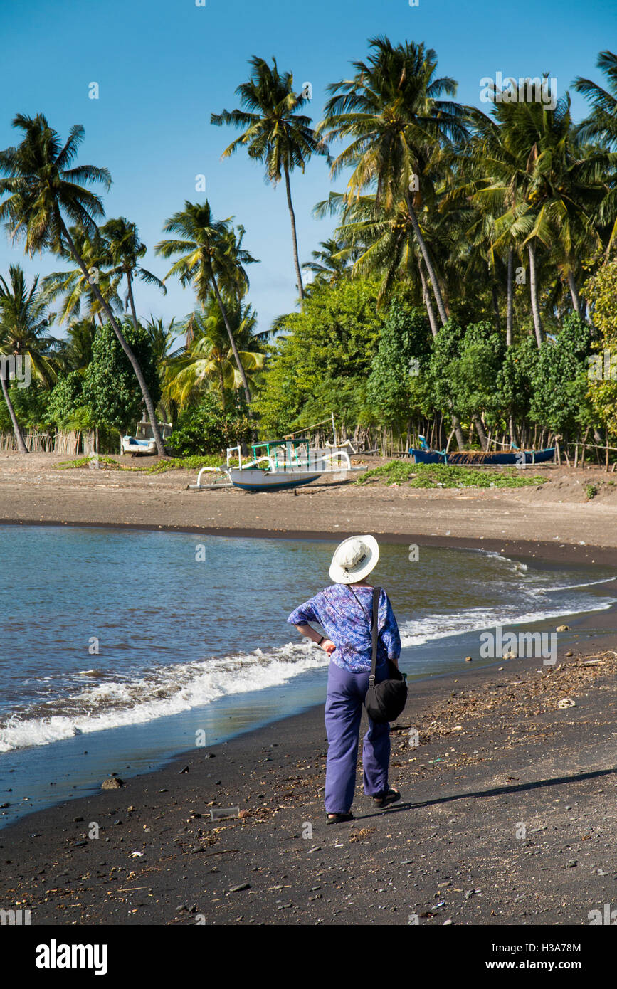 Indonesia, Lombok, Selengan, fishing village, tourist walking on black volcanic sand beach Stock Photo