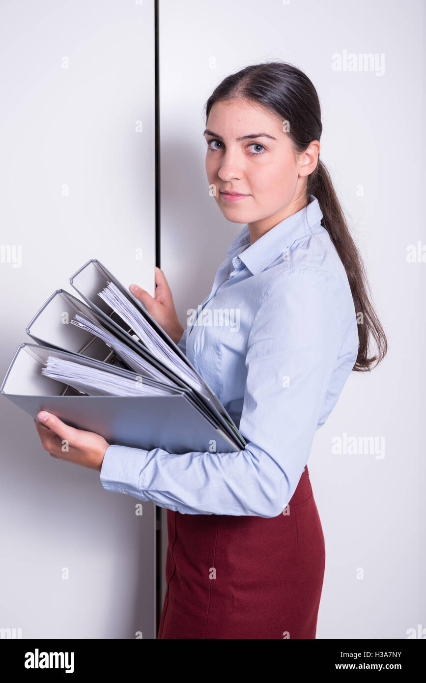 young female professional is putting binders into the Stock