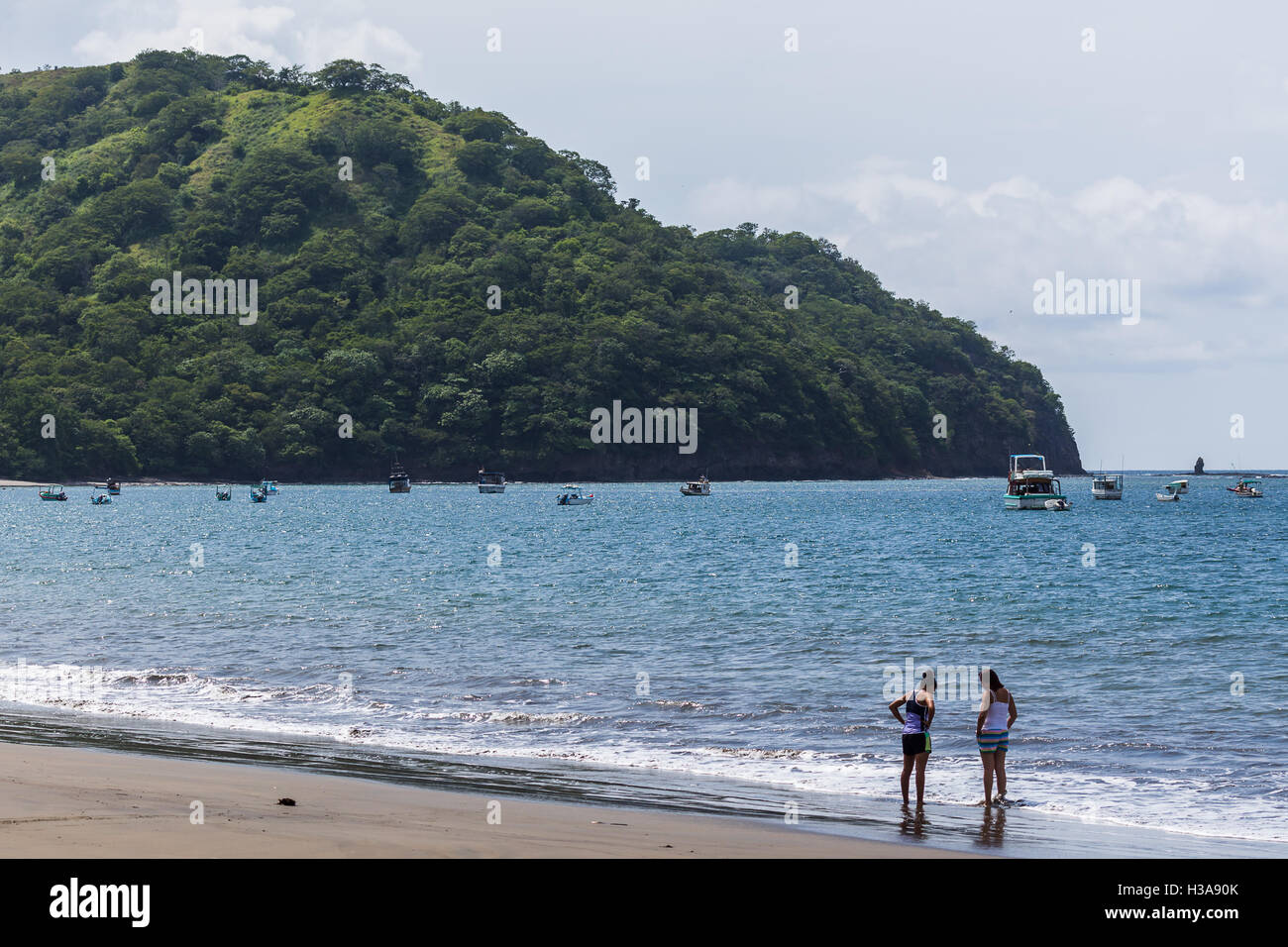 Local people talking on the Coco Beach as private boats occupy the background. Stock Photo