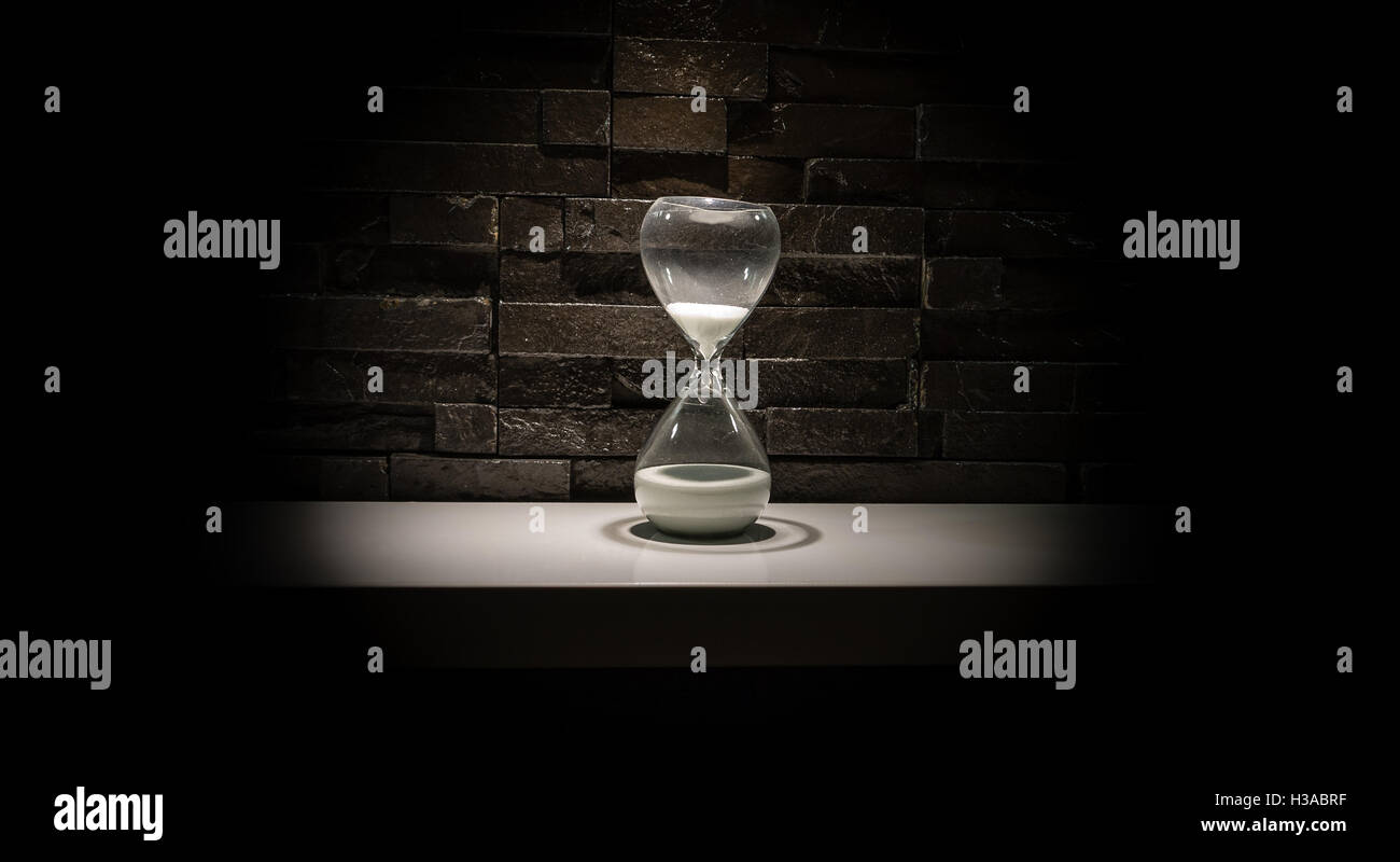 Broken hourglass, sand clock on a dark gray brick wall background Stock Photo