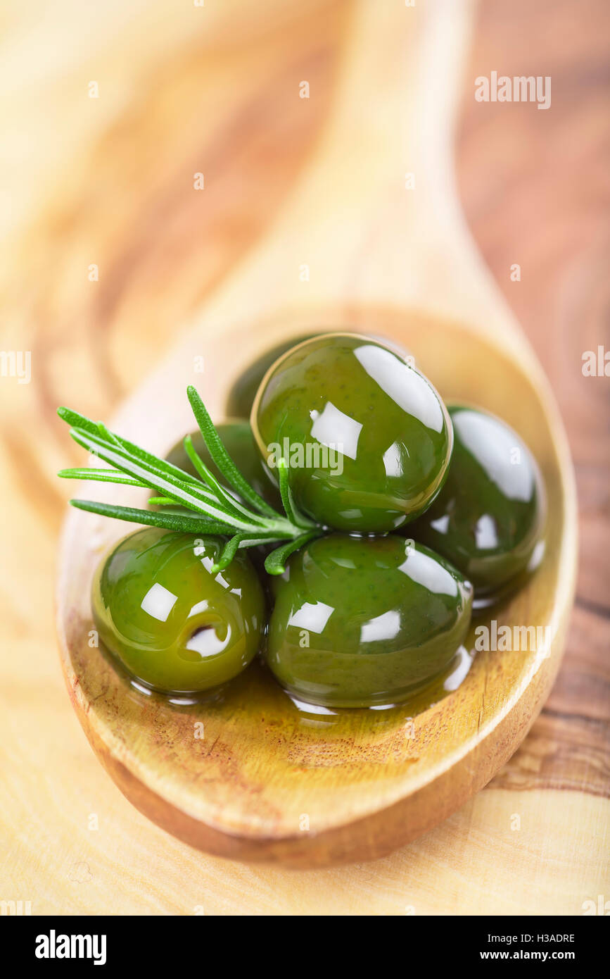 wooden spoon with green olives, olive oil and some fresh rosemary on a ...