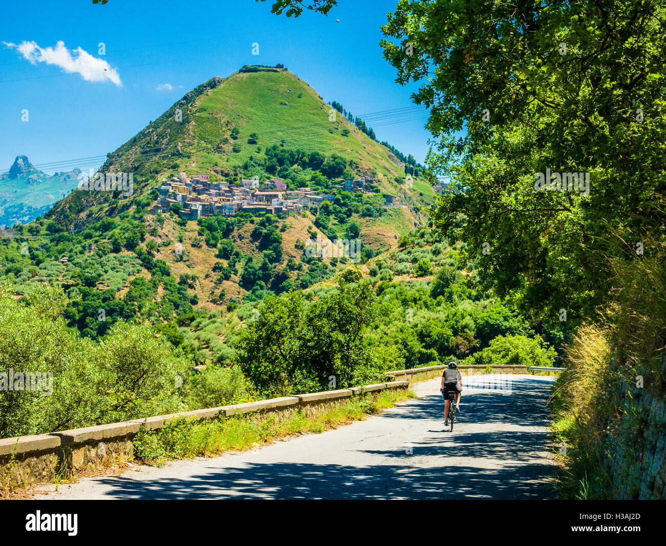 Female cyclist on road approaching Tripi in the Province of Messina, Sicily, Italy Stock Photo