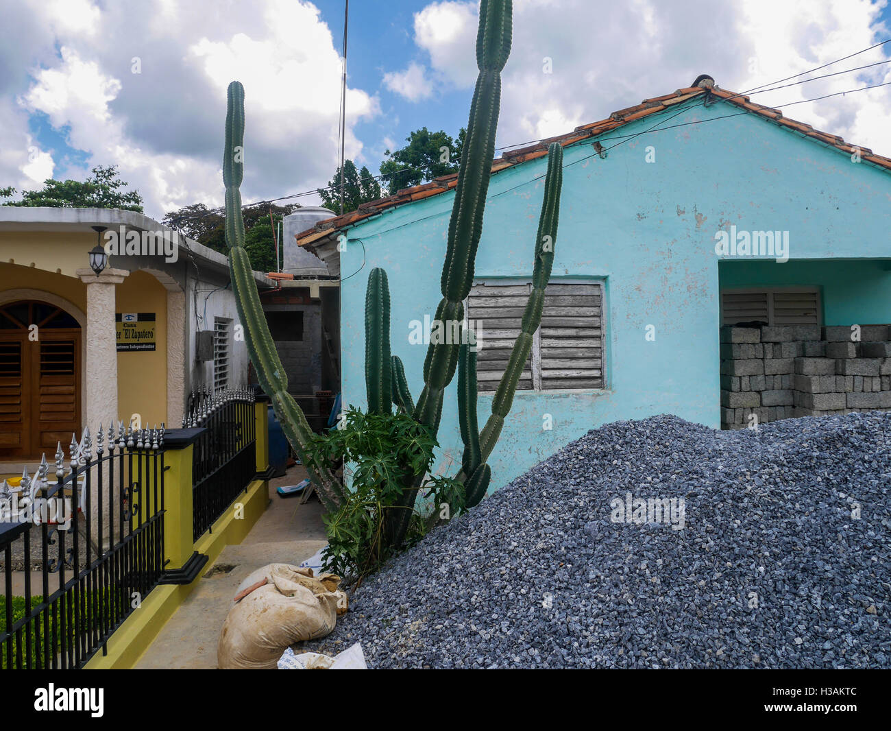 Bright vibrant blue house with a green tall cactus in a backyard, the house is under construction with closed windows and pile of stones in yard Stock Photo