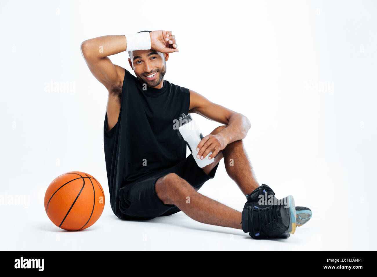 Tired young man basketball player sitting and drinking water over white