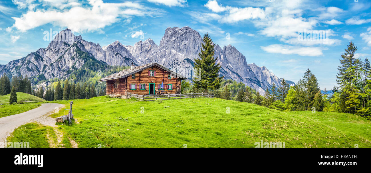 Panoramic view of scenic mountain landscape in the Alps with traditional mountain chalet and fresh green meadows in springtime Stock Photo