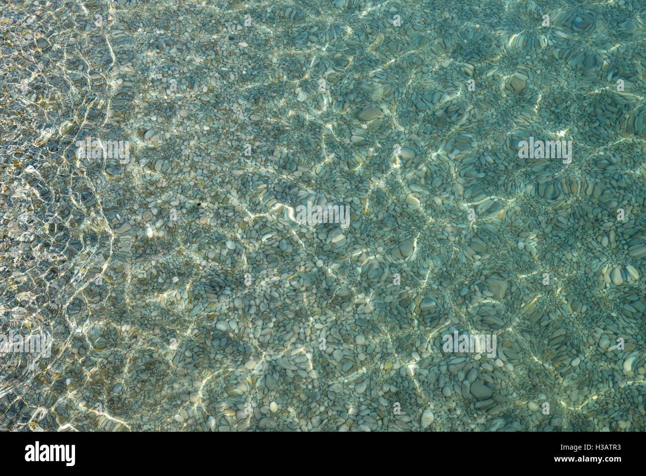 Shimmering sun glares on pebble seabed under clear water of shallow of ...