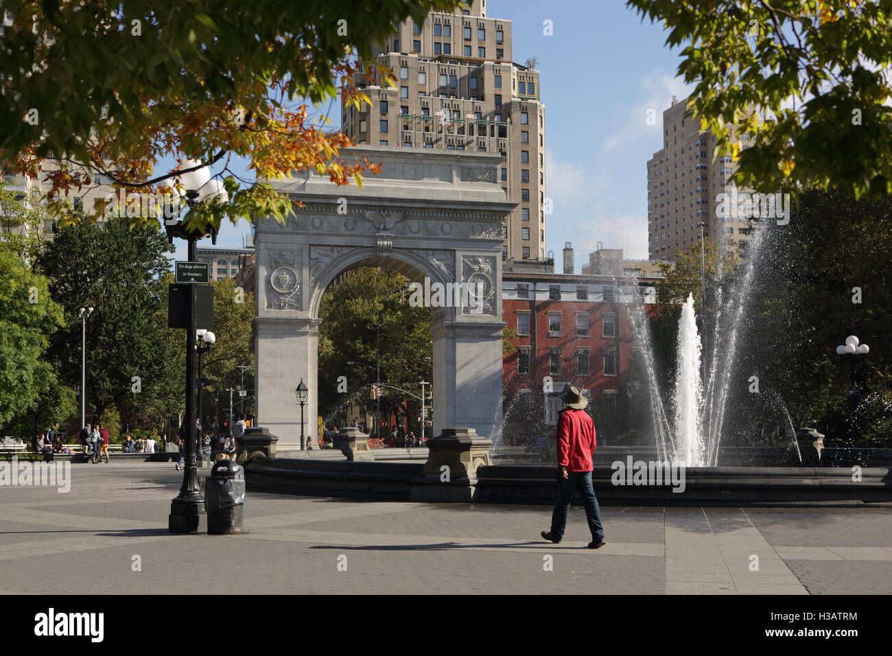 People walk and talk beside the fountain in Washington Square Park, New York. Buildings on Fifth Avenue and the arch can be seen Stock Photo