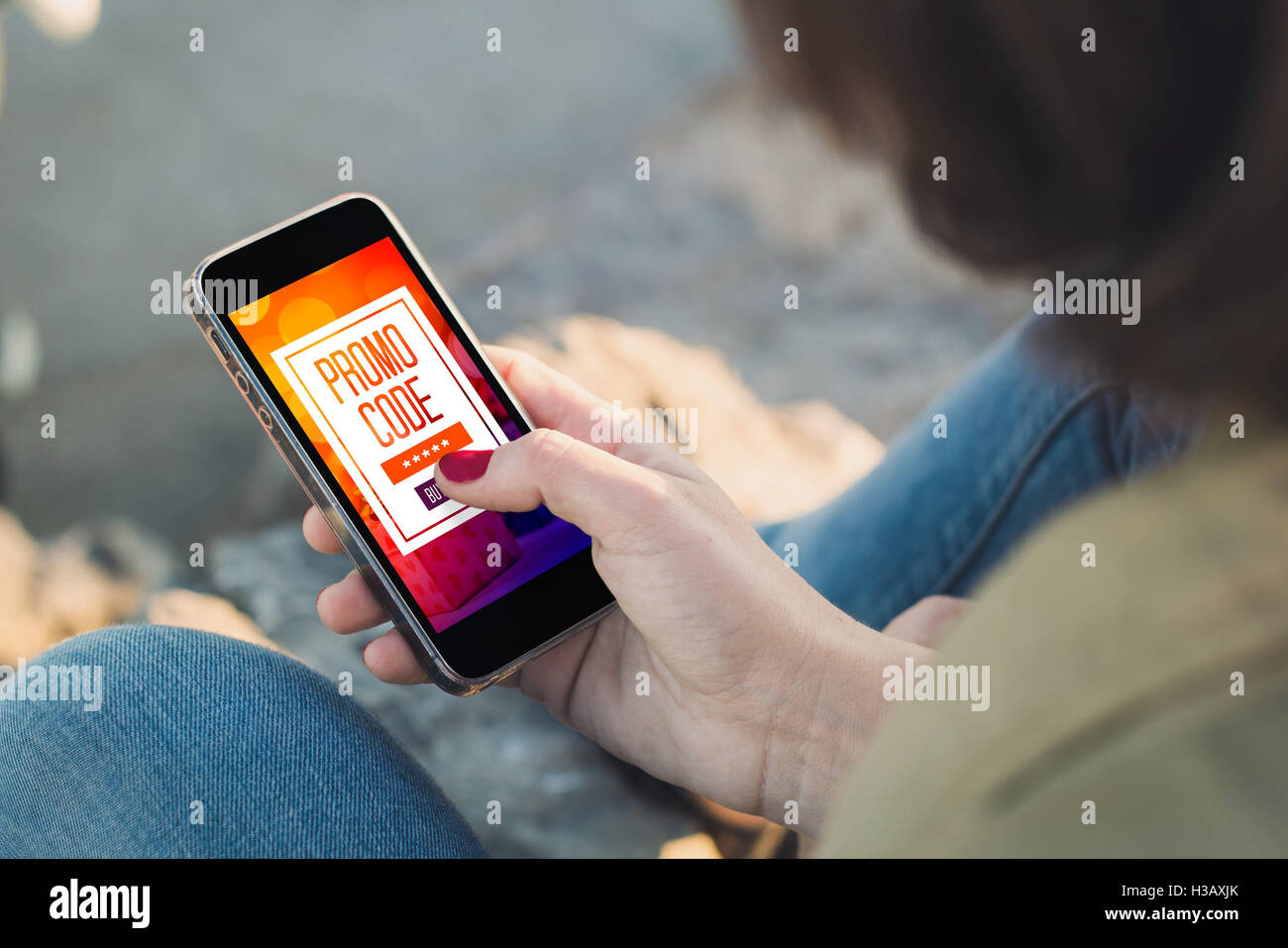 m-Commerce: woman holding a smartphone and buys using a promo code. All screen graphics are made up. Stock Photo